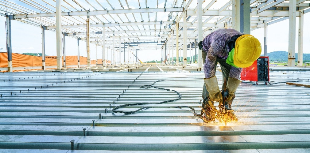 Welder are welds re-bar shear keys metal deck slab of mezzanine floor under the construction building in the factory with blue sky