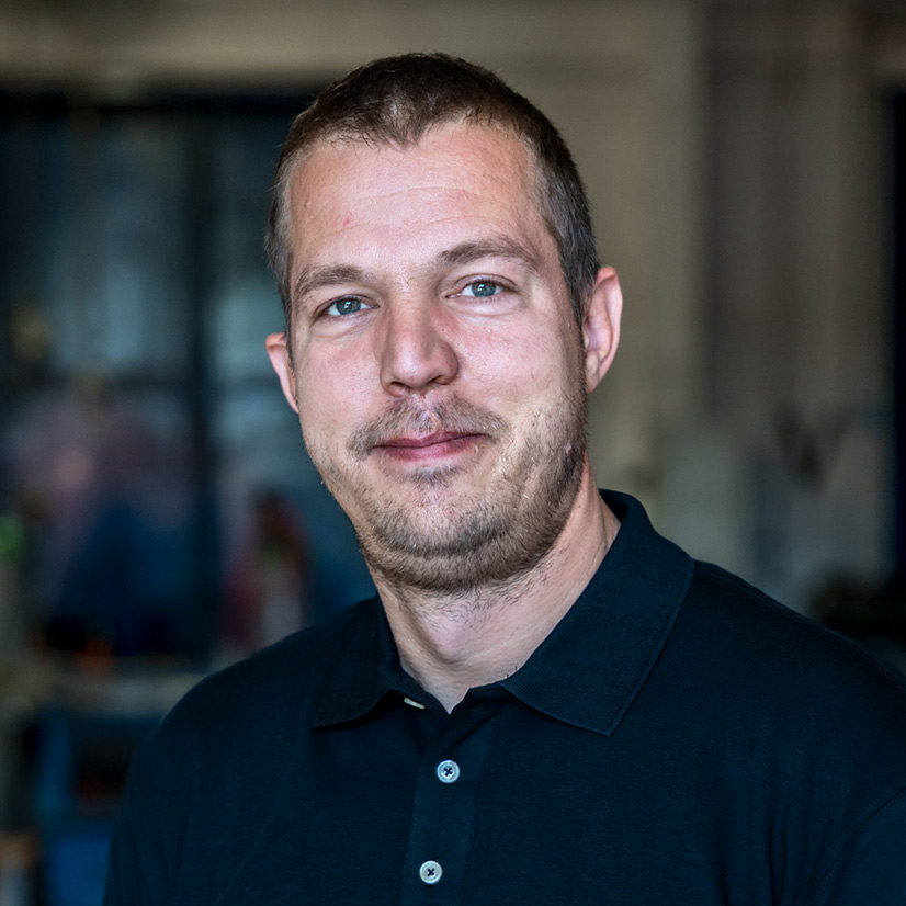 Ein Mann mit kurzem Haar lächelt leicht und trägt ein dunkelblaues Hemd.