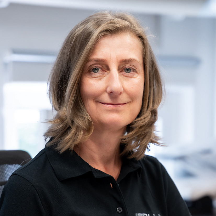 Eine lächelnde Frau mit schulterlangem blondem Haar trägt ein schwarzes Hemd.