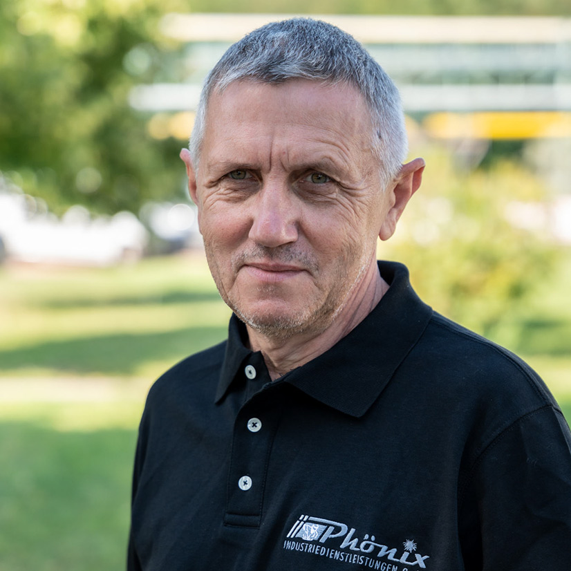 Ein Mann mittleren Alters lächelt leicht und trägt ein schwarzes Poloshirt.