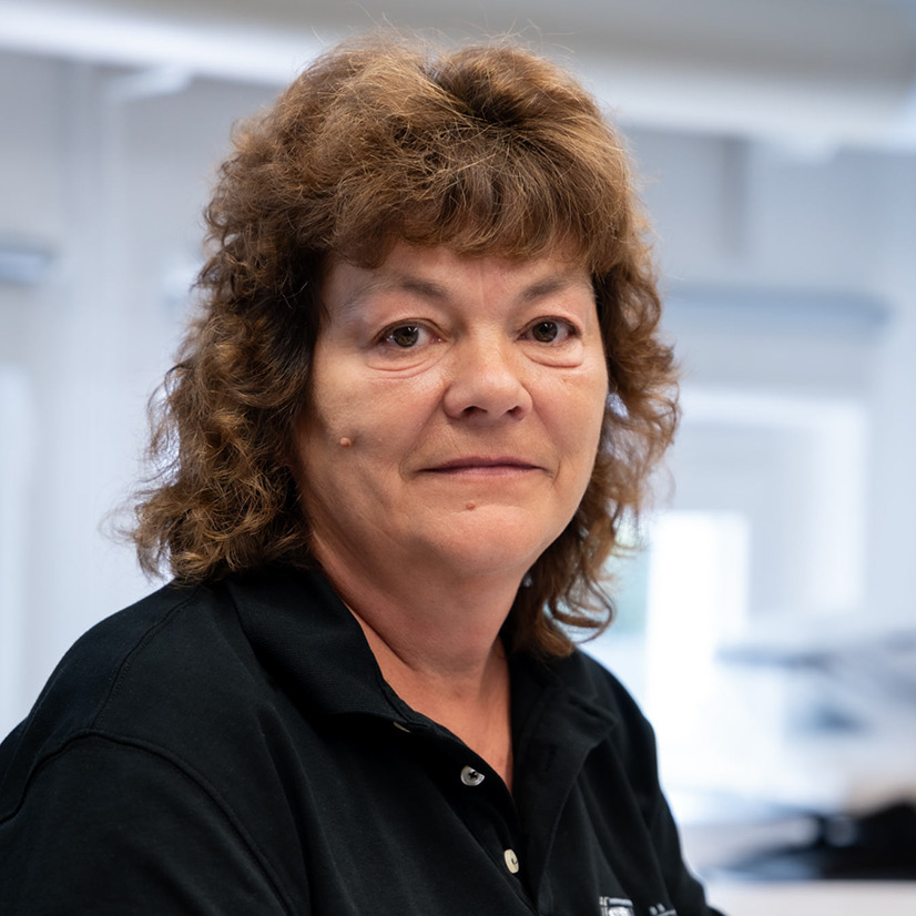 Eine Frau mit lockigem, braunem Haar lächelt leicht und trägt ein schwarzes Hemd.