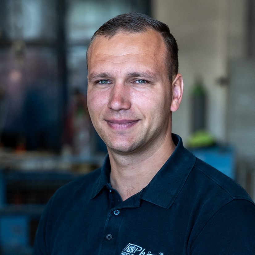 Ein Mann mit kurzem Haar lächelt in einem dunkelblauen Hemd in die Kamera.